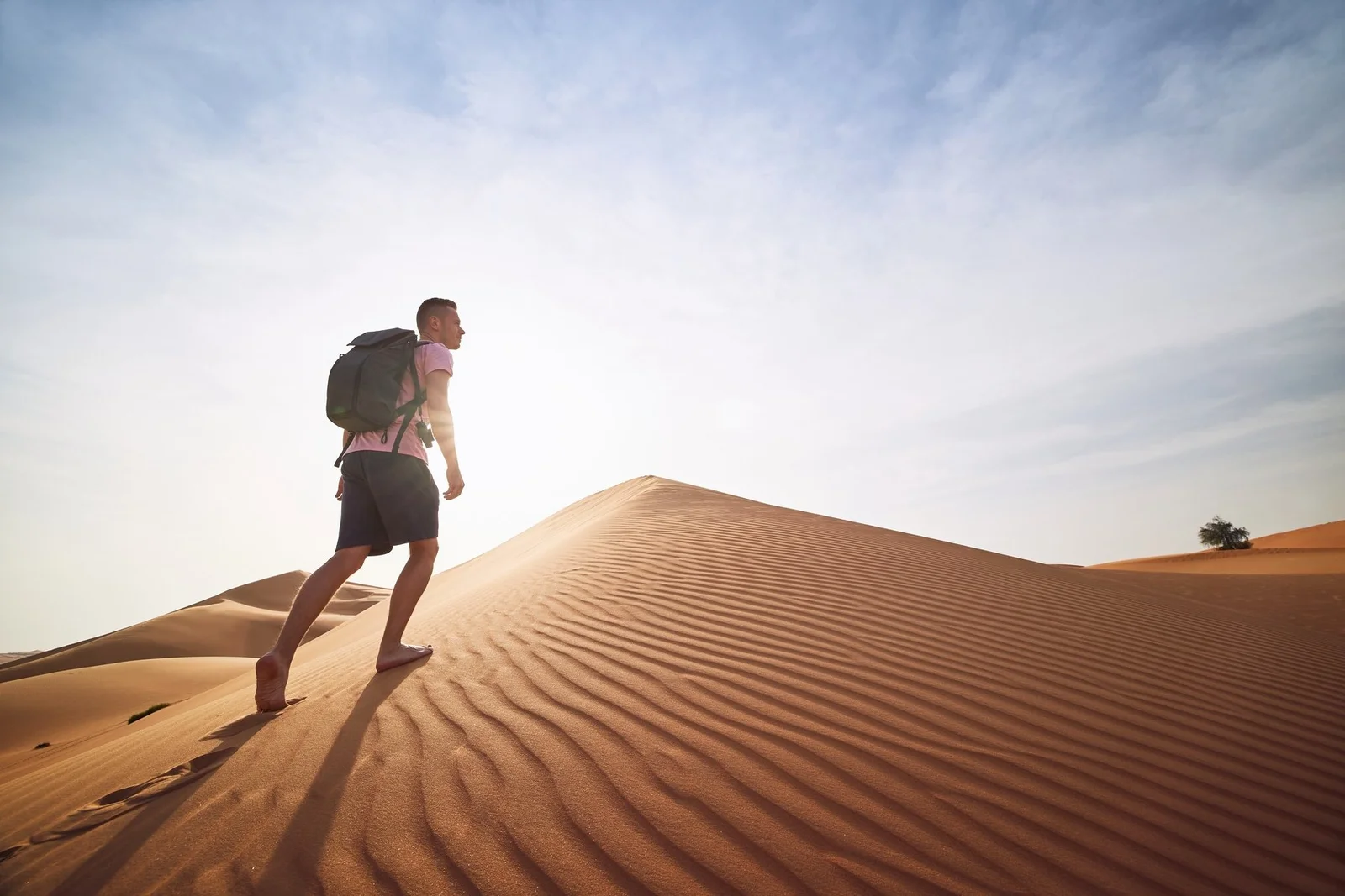 Hiker cresting a dune against the morning sun