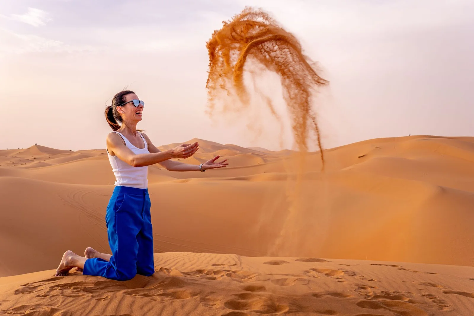 Woman throwing a handful of sand into the air on the dunes